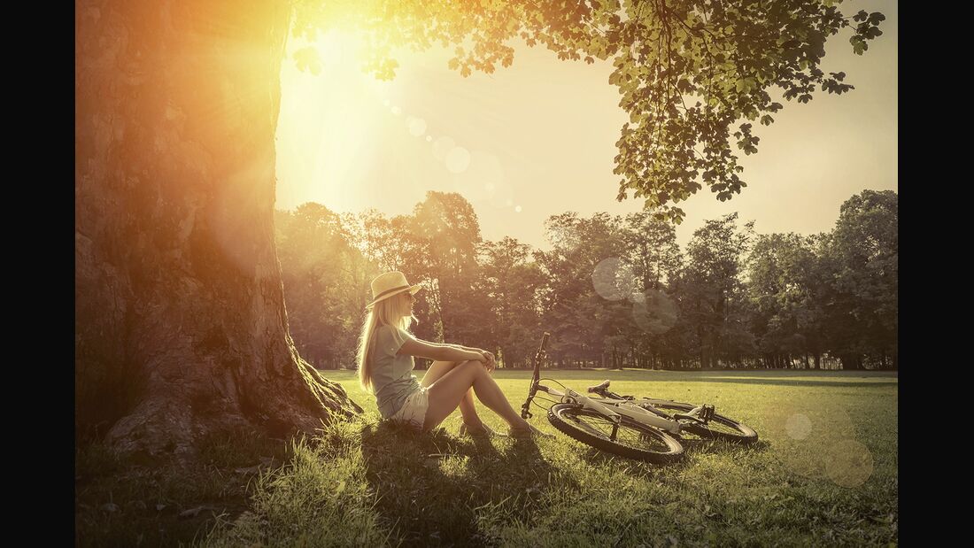 Woman sitting under sun near her bicycle in the park